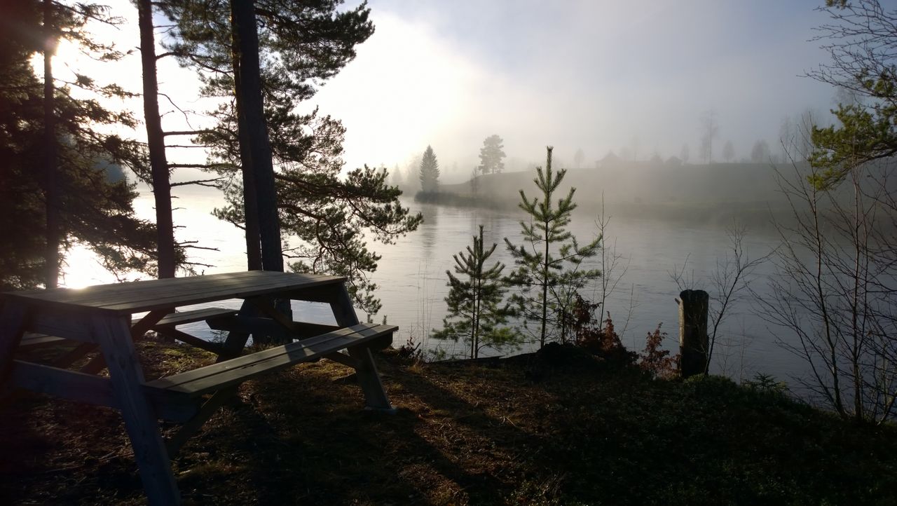Tranquil lakeside scene with fog and bench in Dalarna, Sweden.